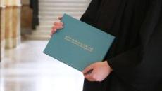 The hands of someone in a graduation gown holding a degree jacket that says Saint Mary-of-the-Woods College.